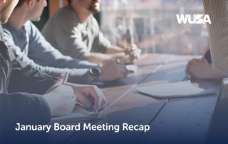 People gathered around a wooden table, diligently taking notes, with "January Board Meeting Recap" elegantly displayed above.