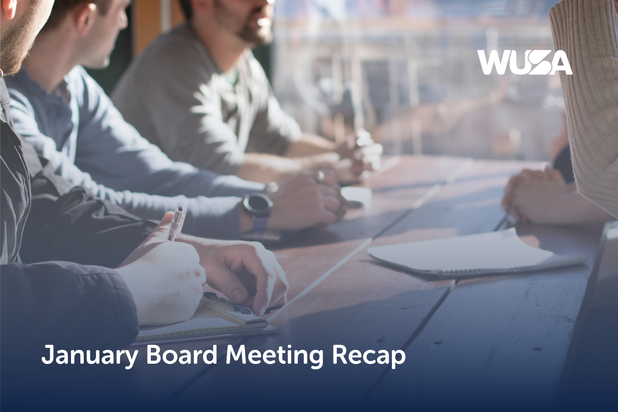 People gathered around a wooden table, diligently taking notes, with "January Board Meeting Recap" elegantly displayed above.