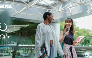 Two students, smiling and holding books, walk confidently outside a modern building adorned with decorative graphics. Their vibrant energy reflects the spirit of a Safer Campus where Your Voice is always heard and valued.