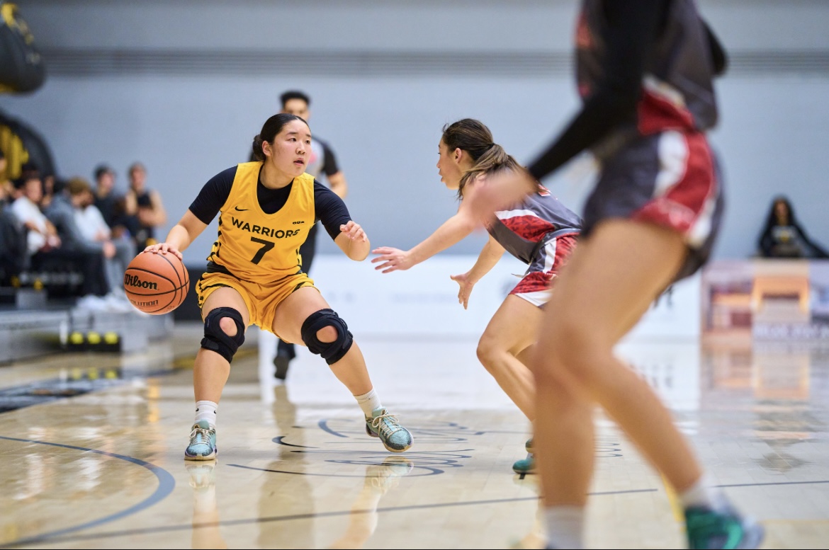 A female basketball player in yellow dribbles while being guarded by an opponent in red on the court during the XChanges 2025 event.
