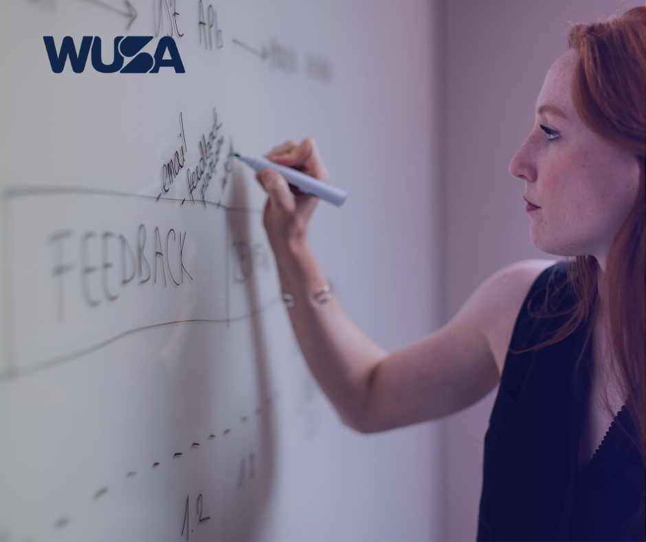 A person writes on a whiteboard with the word "FEEDBACK" prominently displayed, alongside a logo in the corner. This moment captures the essence of provincial advocacy, emphasizing WUSA's commitment to advocating for change.