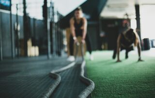 Two people exercise with ropes on a gym's green floor, embodying leadership in sports—one standing strong, the other in a crouched position, synchronized in their empowering pursuit of fitness.