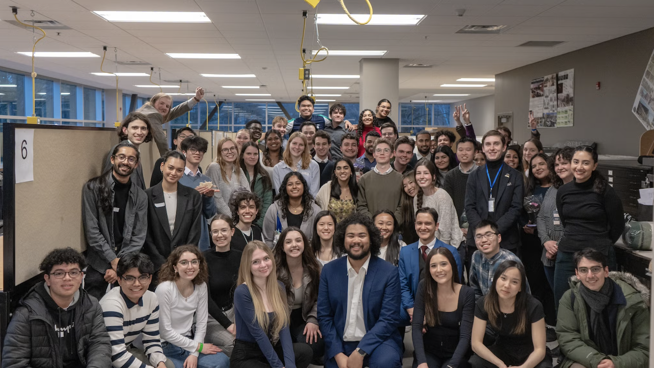 A large group of people smiling and posing together, celebrating the success of their Planning Conference in an office setting.