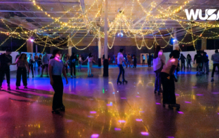 People roller skating under twinkling lights in a rink with colorful floor reflections, the "WUSA" logo gleaming in the corner. It's a Wheels Up night, where excitement rolls with every turn.