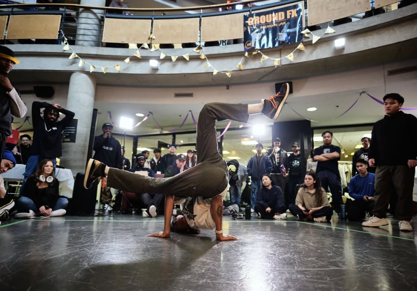 A breakdancer balances on one arm while performing for a crowd in an indoor dance competition.