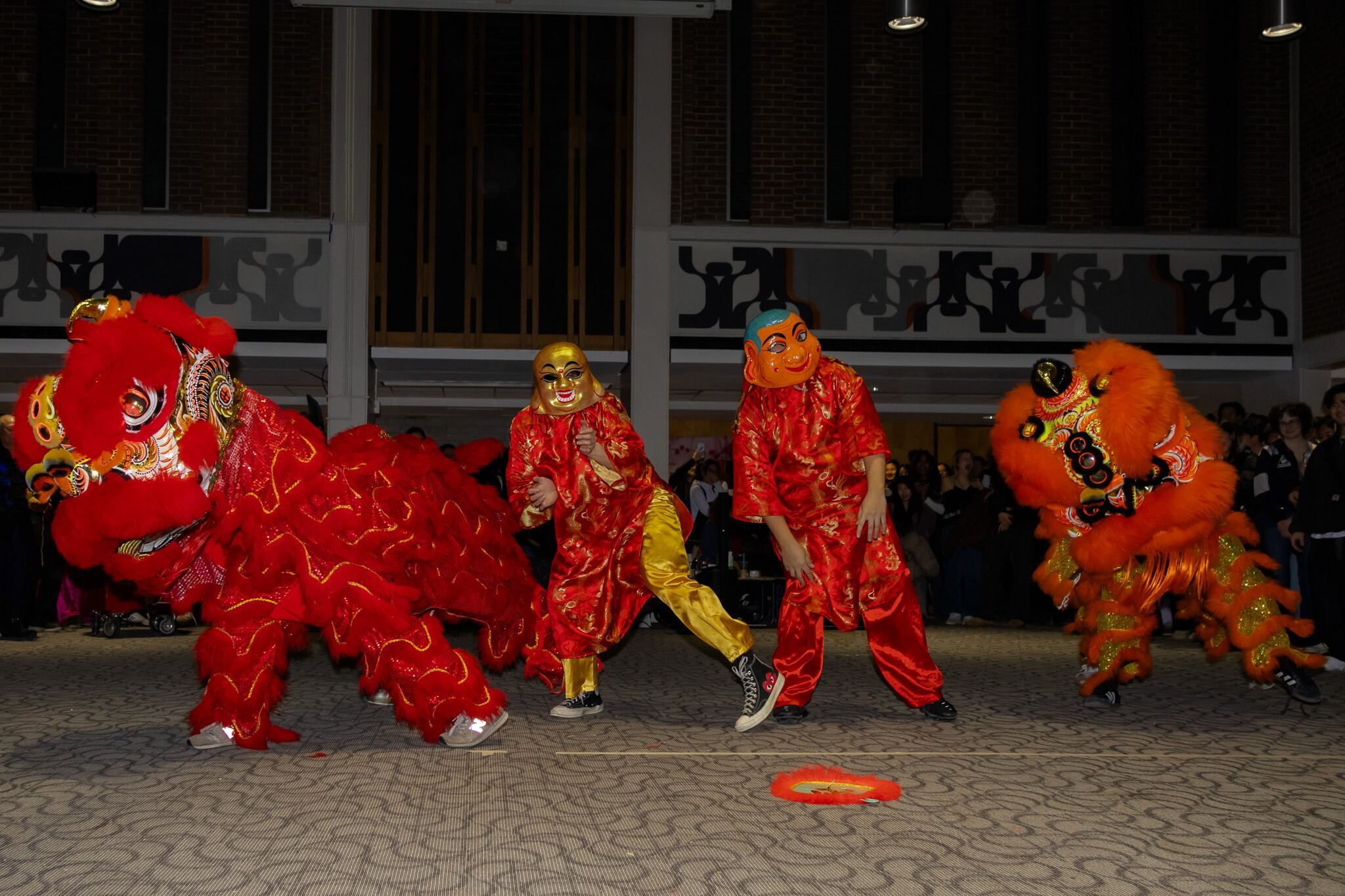 Three performers in lion dance costumes and masks dance indoors during a cultural celebration.