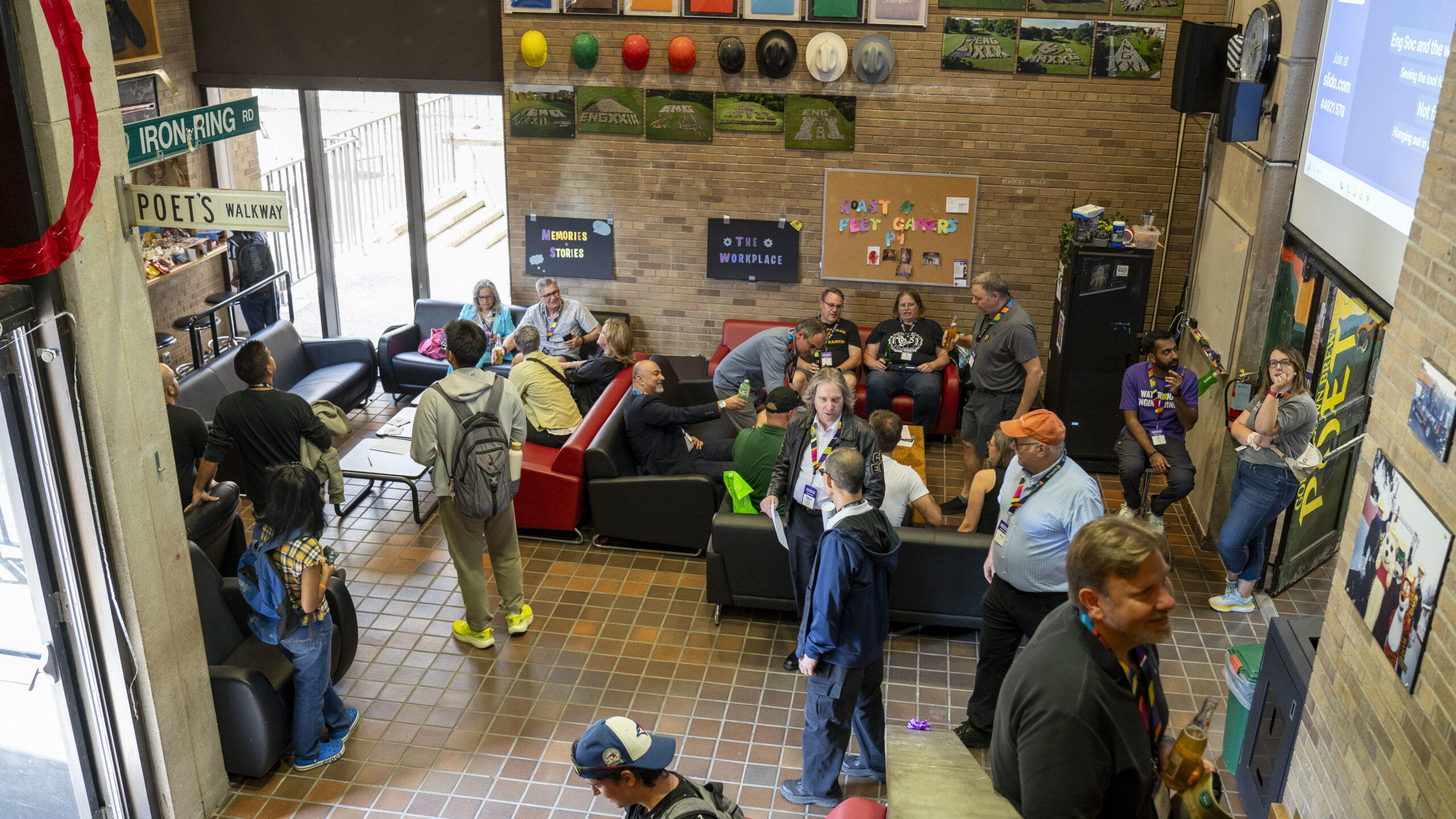 A group of people socializing in a lounge with sofas, wall art, and colorful hats on display.
