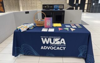 A table with snacks, pamphlets, and signs, covered by a WUSA Advocacy cloth in a building lobby, raises awareness for Sexual Violence Month.