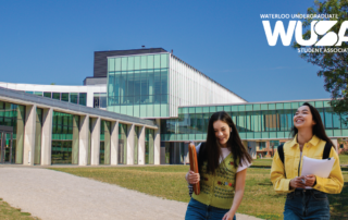 Two students walk and smile outside a modern glass university building under a clear blue sky, ready for Waterloo Ready. WUSA logo in corner.