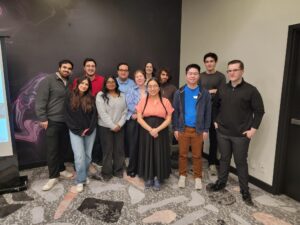 A group of thirteen Student Leaders posing together and smiling in an indoor setting with a dark wall behind them, showcasing their involvement in student leadership.