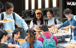 Students gather around tables at the Welcome Brunch, selecting pastries and food, smiling and socializing at this lively campus event.