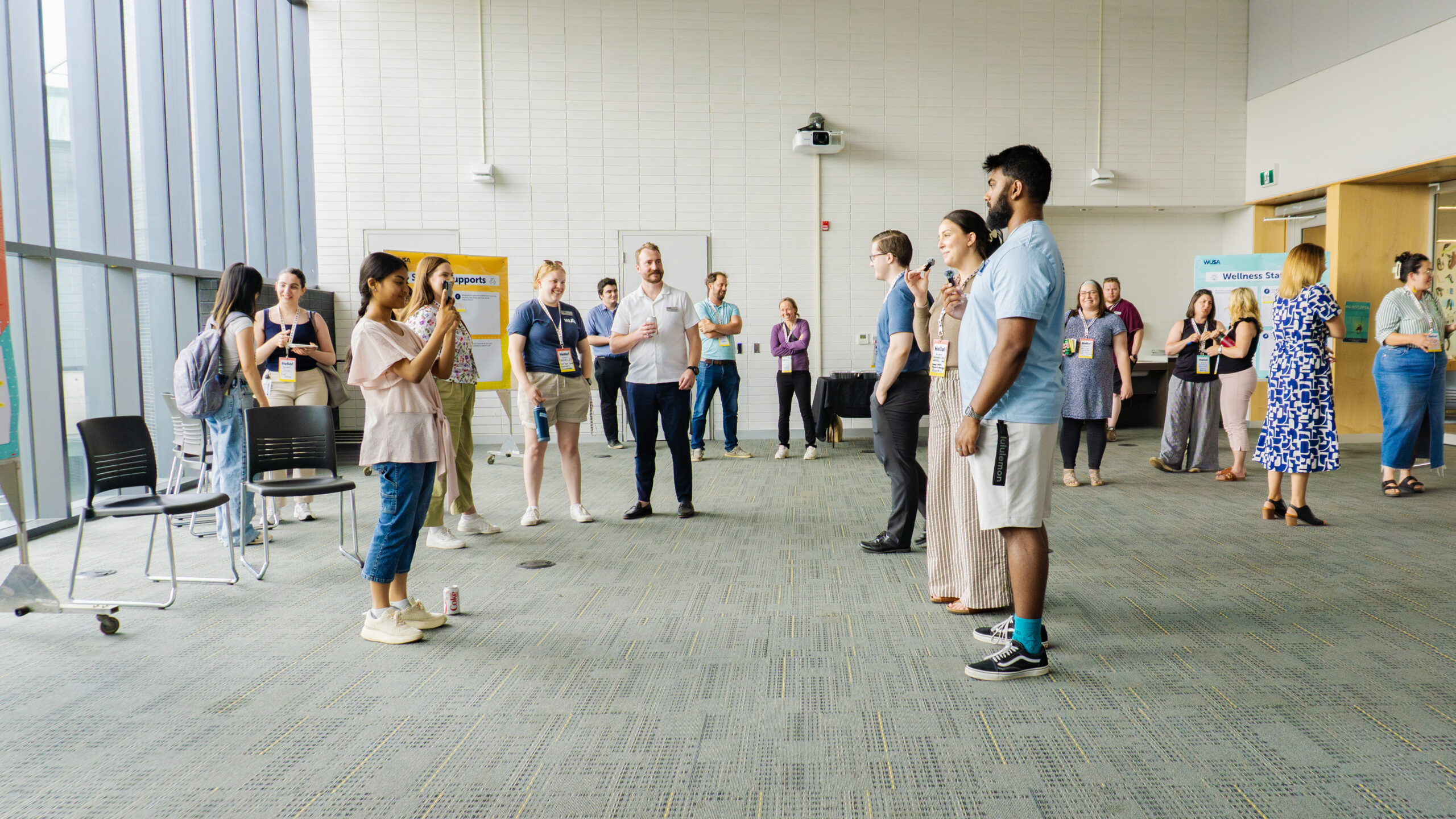 A group of people stand and talk in a bright, modern room during a casual event or workshop.