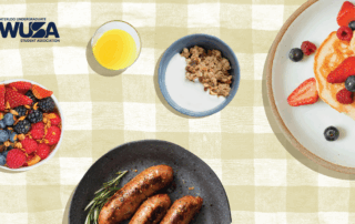 A Welcome Brunch spread features sausages, pancakes with berries, granola, juice, and a berry parfait on a checkered cloth.