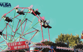 A Ferris wheel and Tilt-A-Whirl ride at the Welcome Week Carnival, with trees and a clear blue sky in the background.
