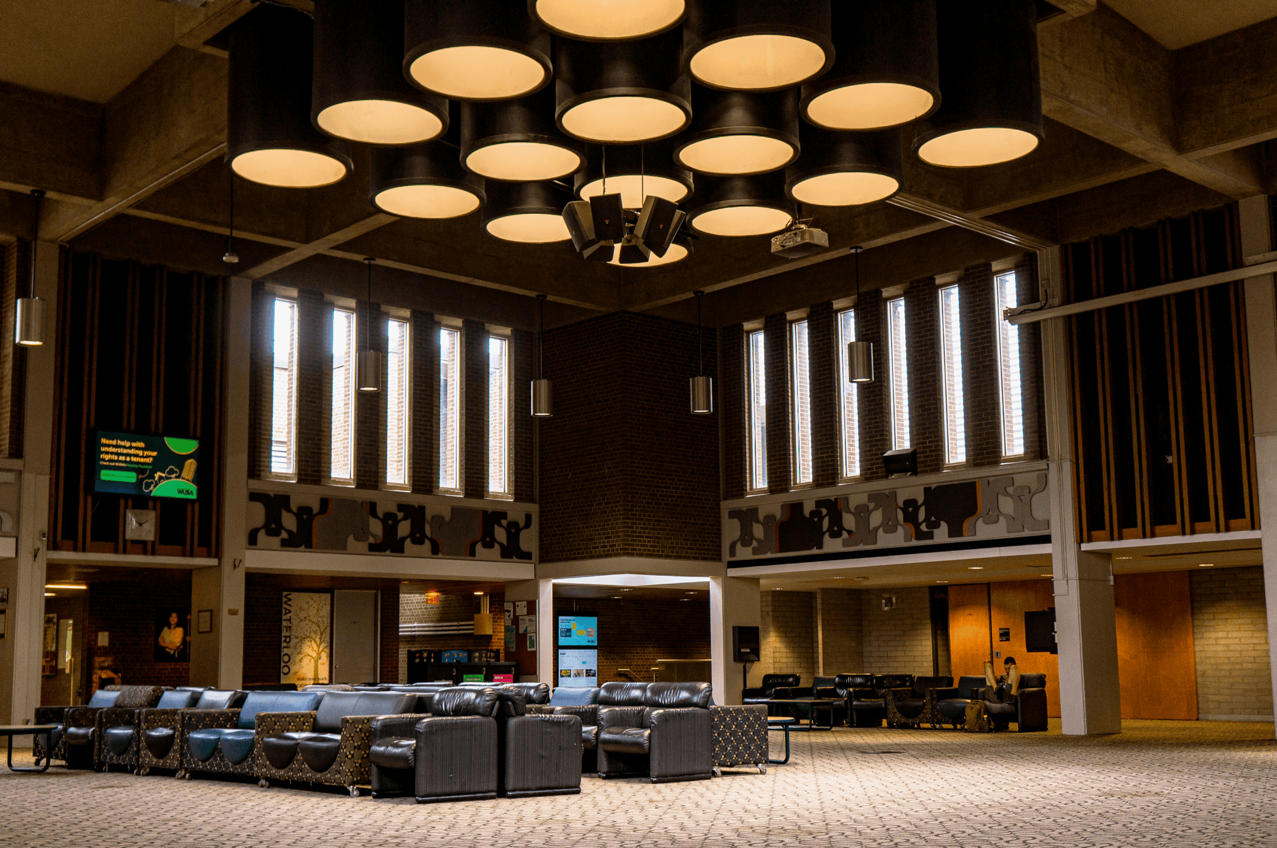 Spacious lobby at the Student Life Centre with modern furniture, large ceiling lights, and tall windows letting in natural light.