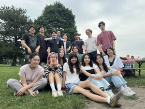 A group of sixteen young adults, recognized for Student Excellence, pose and smile together outdoors on grass near a picnic table during the WUSA Volunteer Awards in Spring 2025.