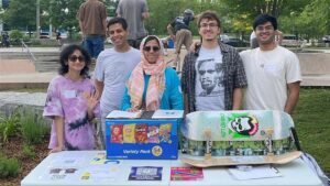 Four people stand behind a table with snacks and a skateboard at an outdoor event in a park, celebrating Student Excellence at the WUSA Spring 2025 Volunteer Awards.