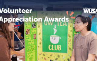 Two students talk at an event booth for OWL TEA CLUB, with a WUSA Volunteer Awards banner celebrating Student Excellence above.