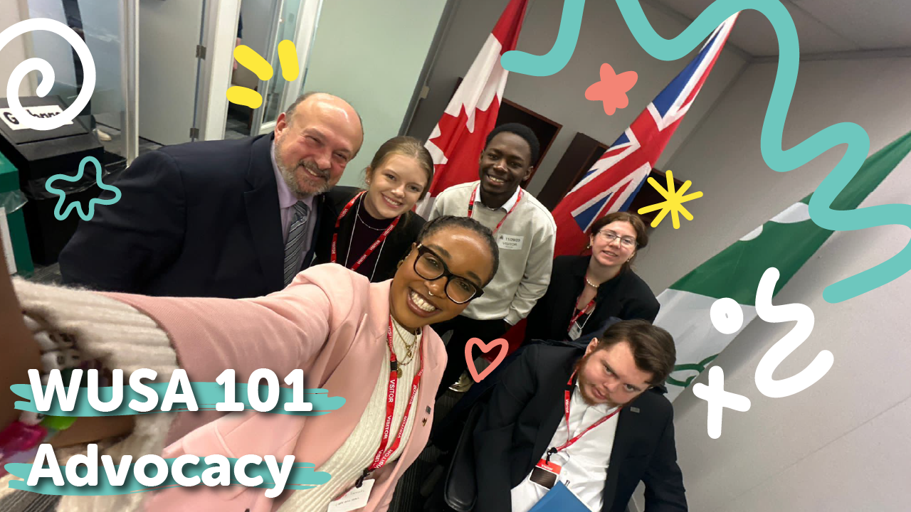 Six smiling people pose for a selfie in an office with flags and playful doodles. Text reads "WUSA 101 Advocacy".