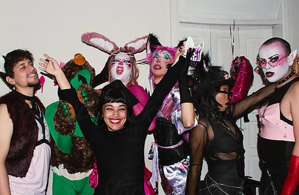 A group of people in colorful, creative costumes pose playfully together in front of a white wall, celebrating Fruity Fright Night fun that's perfect for all ages.