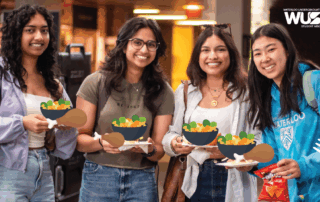 Four smiling students holding illustrated bowls of salad at a satellite campus luncheon, WUSA logo visible in the corner.