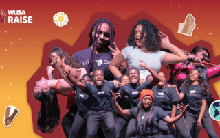 A diverse group of people dance energetically on stage at the Raise Cultural Caravan, surrounded by colorful stickers and a vibrant red-orange background.