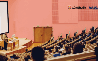 A lecturer, recipient of the Accessible Teaching Award, speaks to students in a large, pink lecture hall at the University of Waterloo.