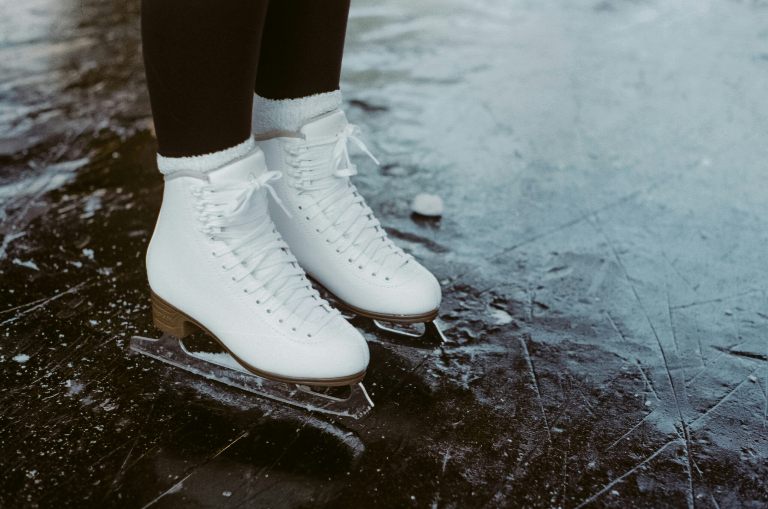 Close-up of a person wearing white figure skates standing on an outdoor ice rink, ready for a fun Skate Social inspired by the skateboarding community.