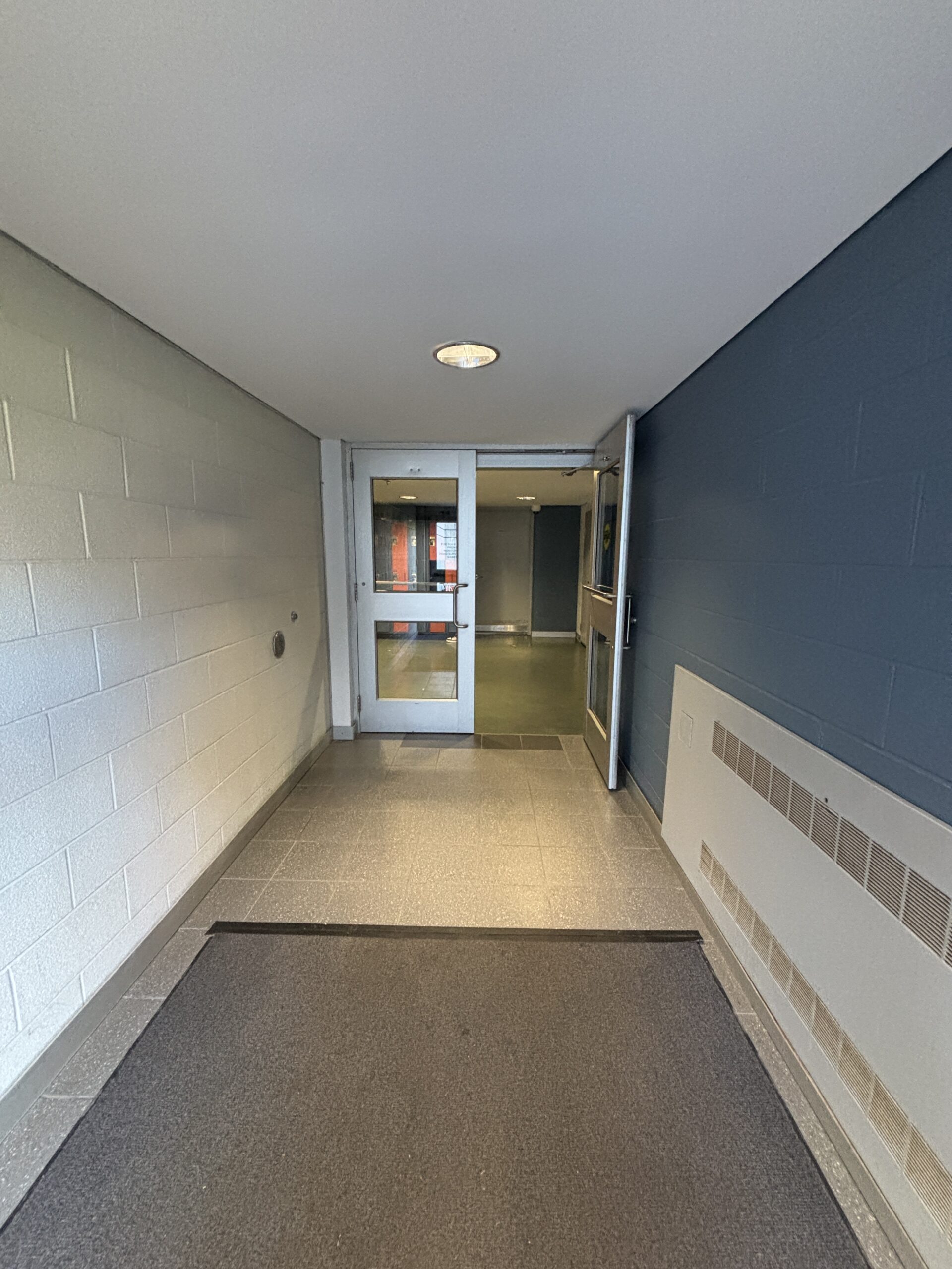 A hallway with gray walls and tile floors leads to a glass door and another hallway beyond, inviting you to discover more as you visit SLC.