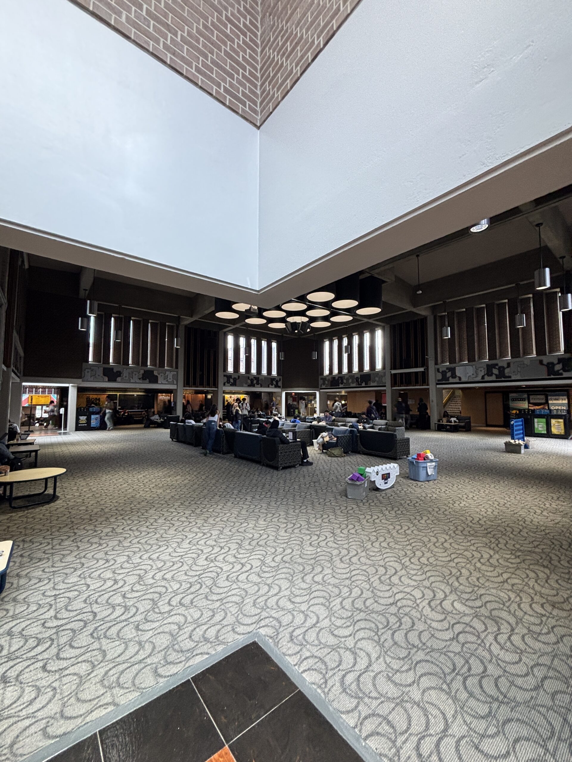 A spacious SLC lobby with sofas, people sitting, and modern ceiling lights, under high windows and brick walls.