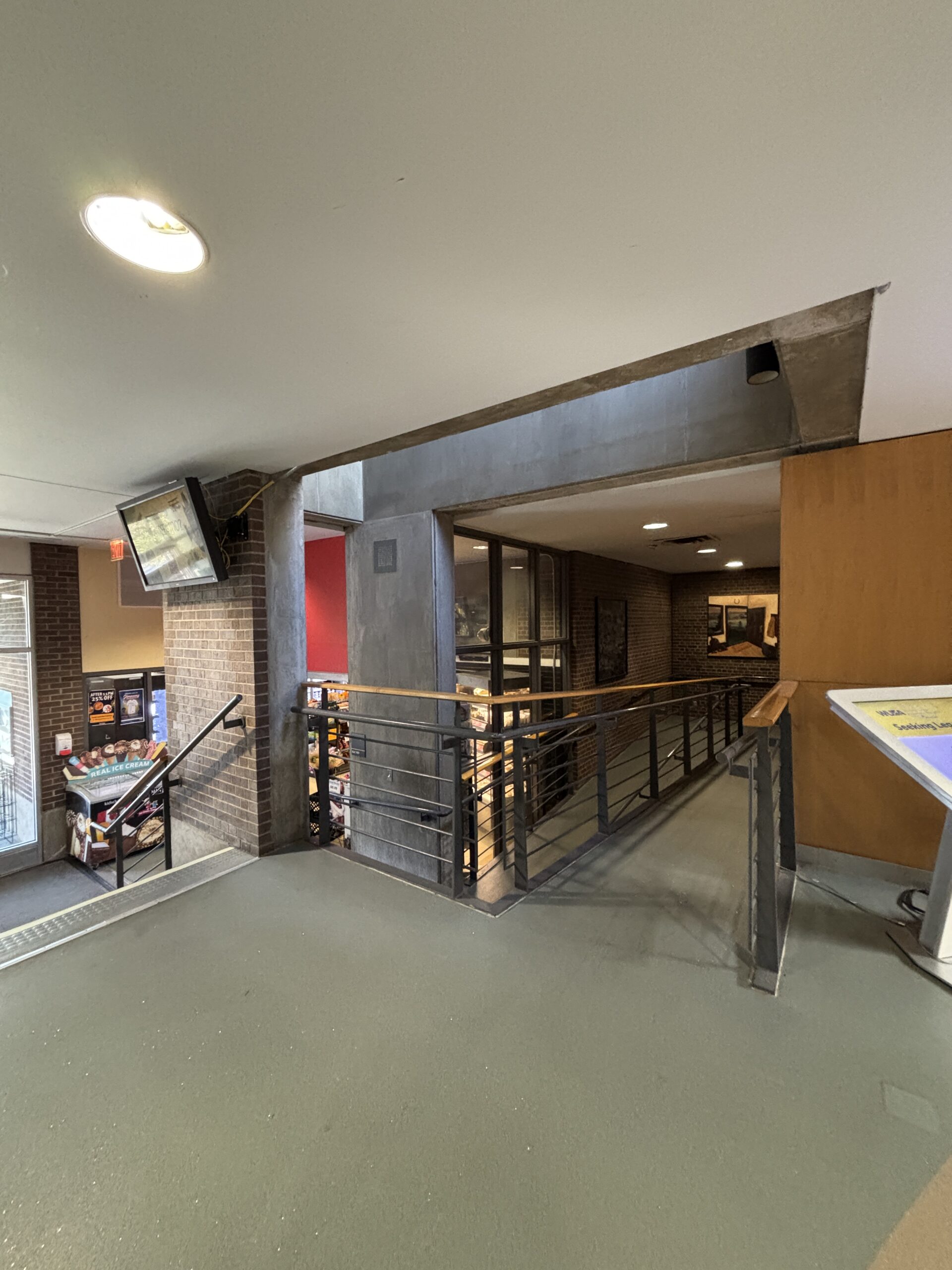 Ramp with black railing leads to glass doors at the SLC; TVs and posters are visible on brick walls in the background.