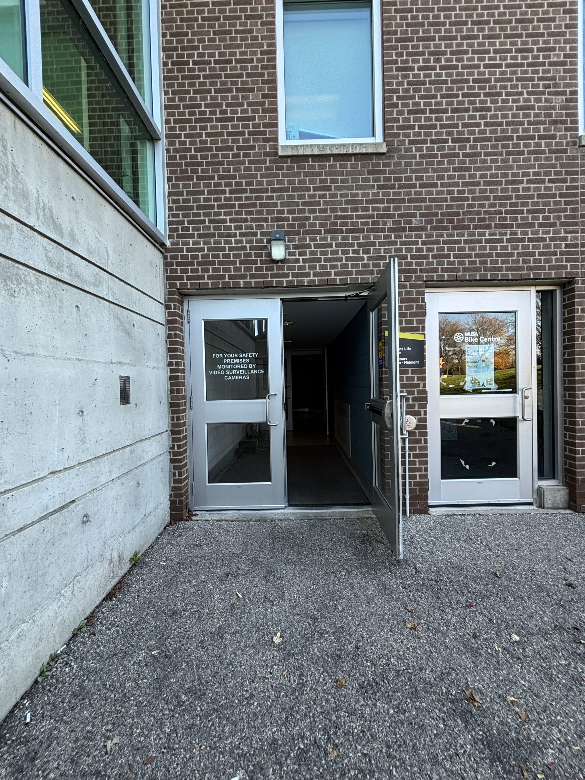 A brick building entrance with double glass doors, one open, leads into a dimly lit hallway at the SLC.