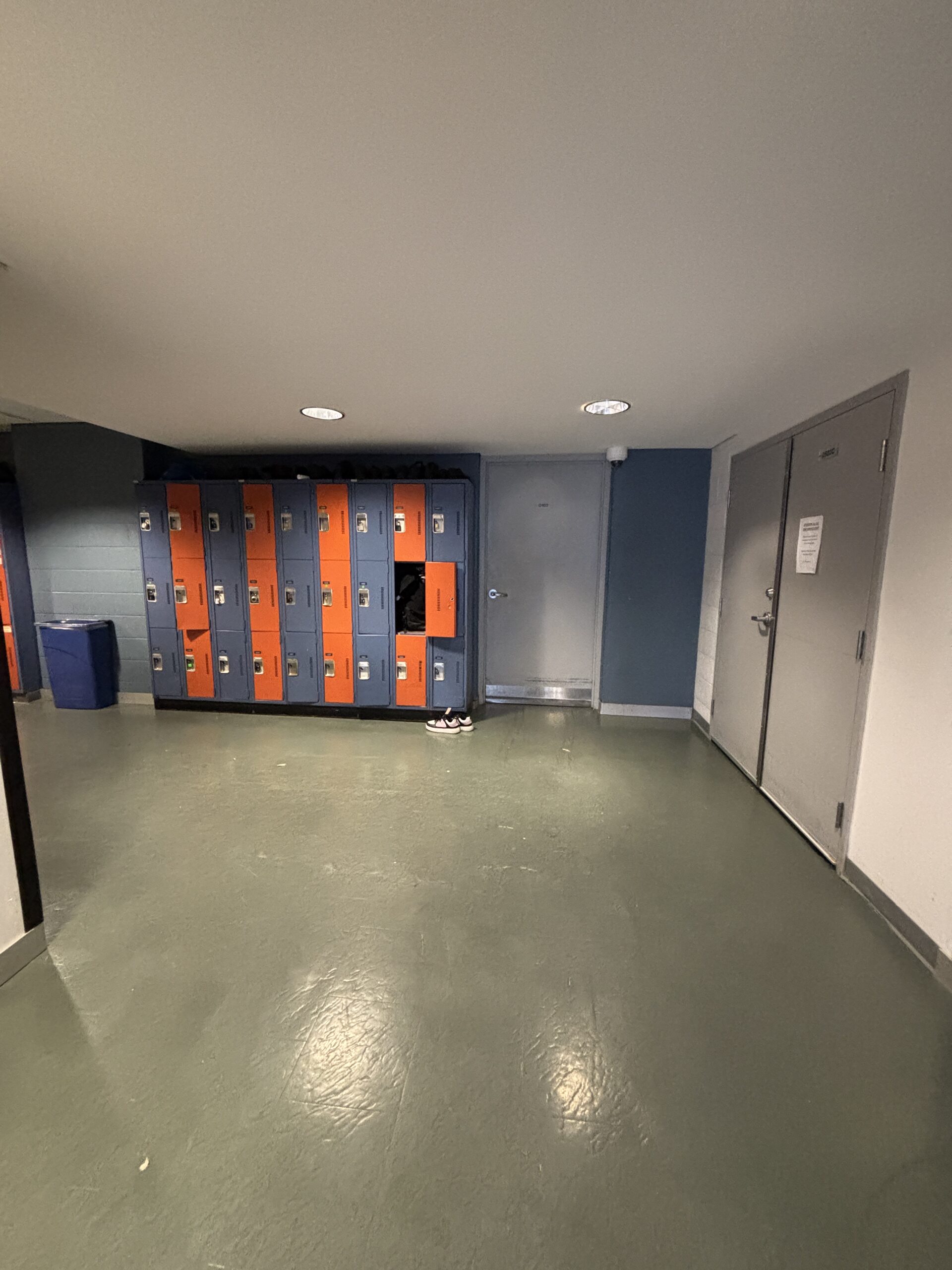 Orange and gray lockers stand against a wall in the SLC, with a pair of black shoes on the floor in front of them.