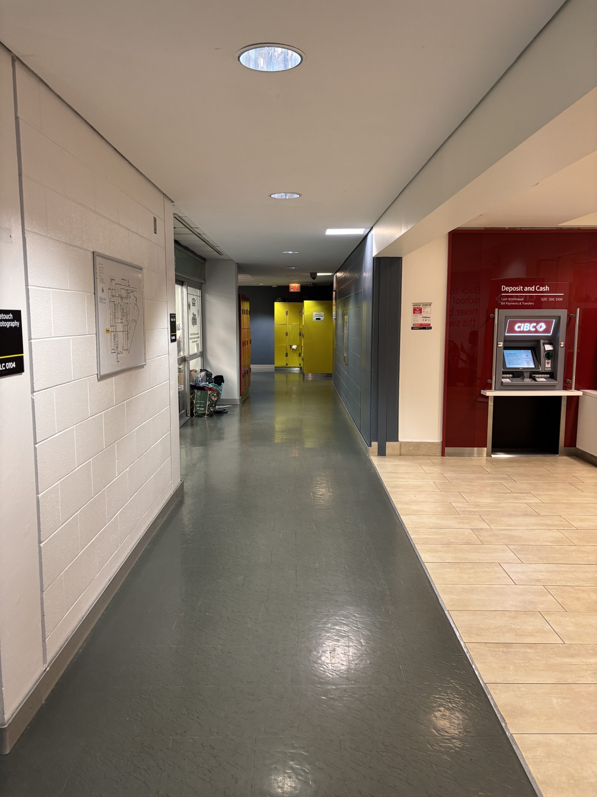 A hallway with gray floors, a yellow door at the end, and a red ATM on the right wall leads to the Student Learning Center (SLC).