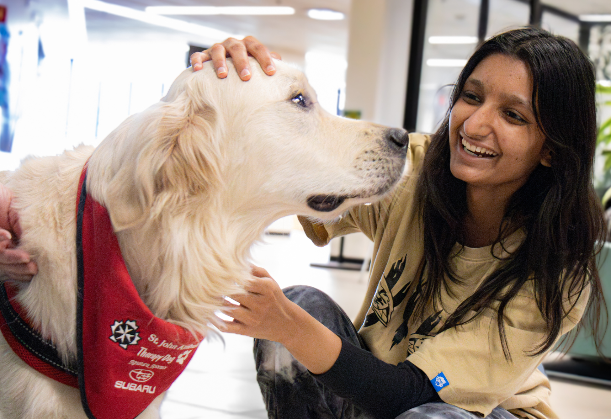 Smiling woman pets a white emotional support dog wearing a red bandana indoors.