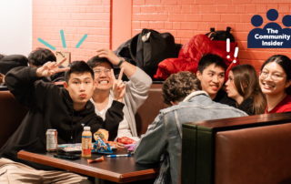 A group of friends laugh and pose together at a table with snacks, under a sign reading "The Community Insider," celebrating their feature in the latest WUSA Community Insider Email.