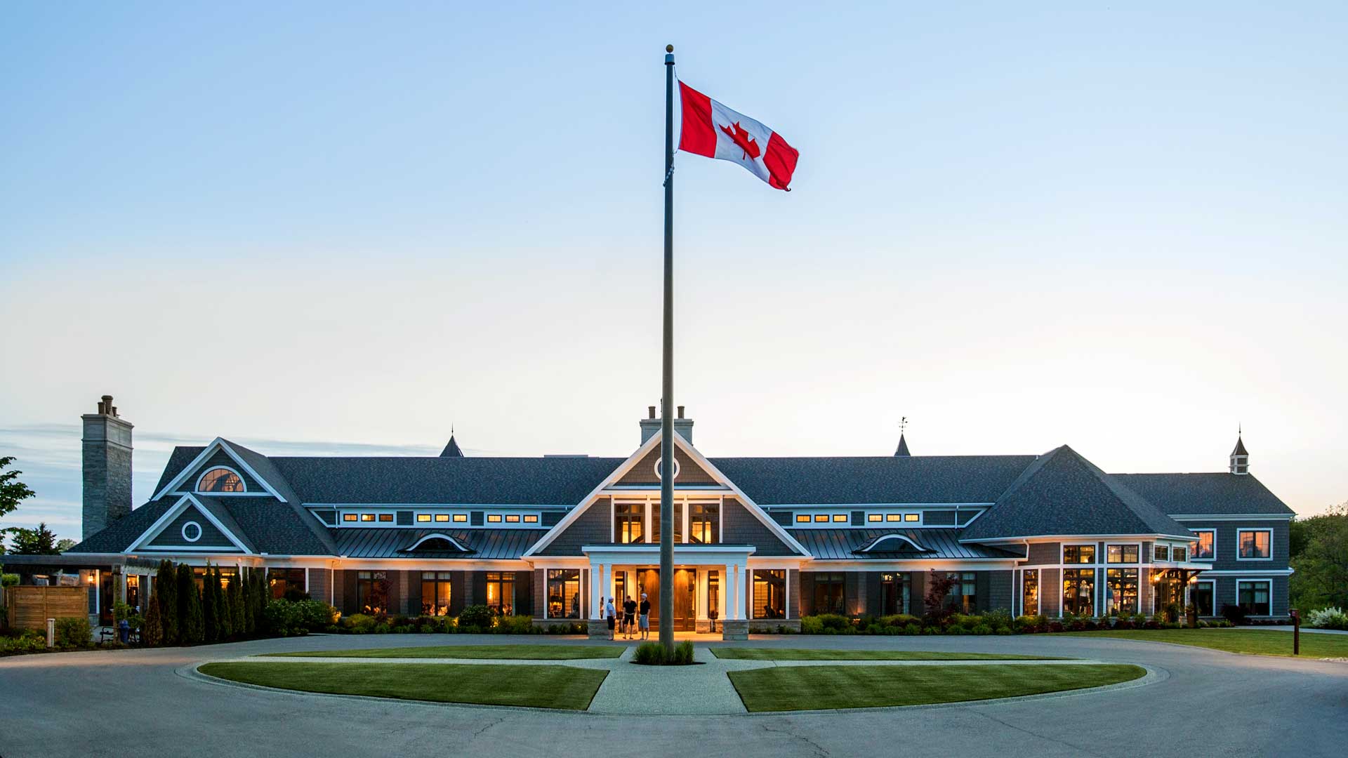 Large building with a peaked roof and a Canadian flag on a tall pole in front, at sunset—capturing the spirit of the University of Waterloo as it prepares for its annual GALA.