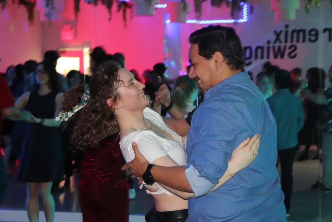 Two people smiling and dancing closely together in a lively, colorful party setting at the UW Salsa Club’s End of Term Social, celebrating with vibrant Cuban Salsa moves.