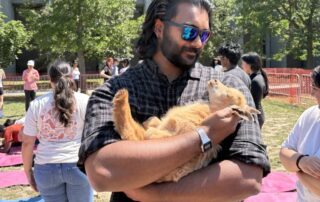 Man in sunglasses holds a small brown goat outside, highlighting his co-op experience with WUSA, with people and trees in the background.