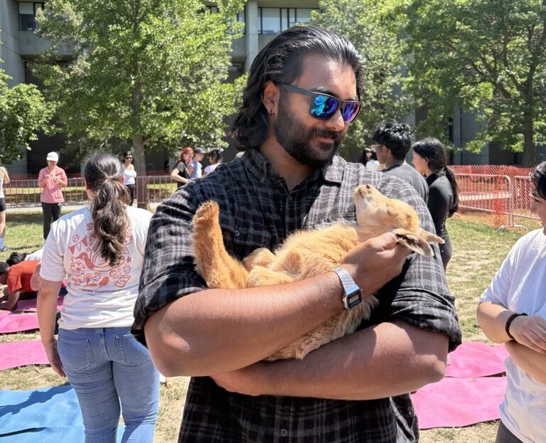 Man in sunglasses holds a small brown goat outside, highlighting his co-op experience with WUSA, with people and trees in the background.