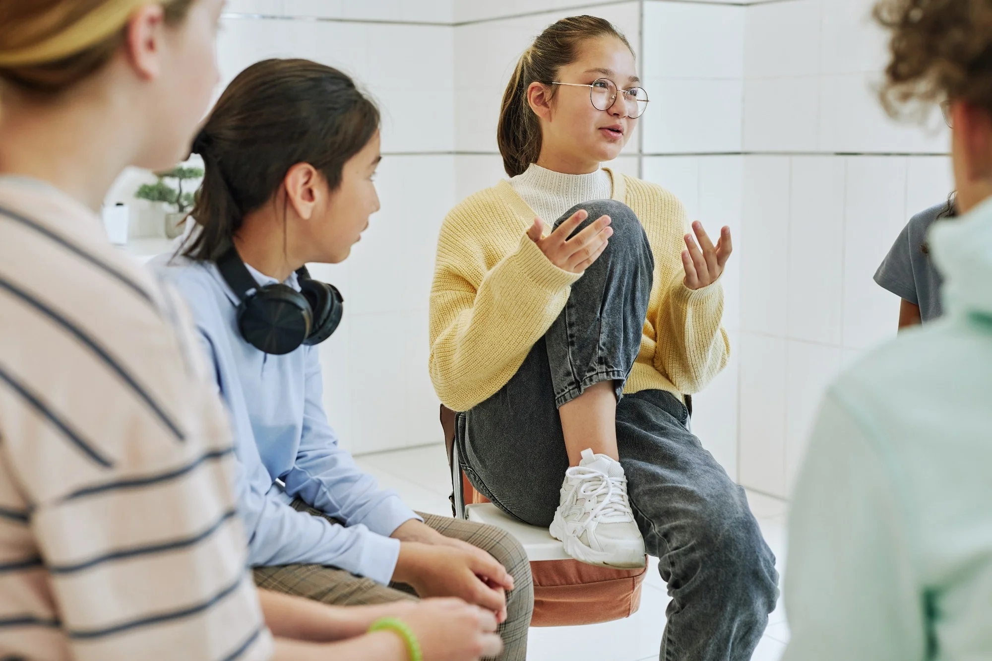 A girl in glasses speaks animatedly to a group of kids sitting in a circle in a bright room, helping her mates gain a better understanding of stress and how our bodies respond to it.