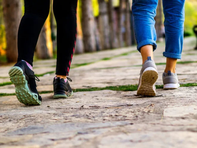 Two mates walking on a stone path outdoors, shown from behind, focusing on their legs and shoes—enjoying a peaceful wellness walk together.