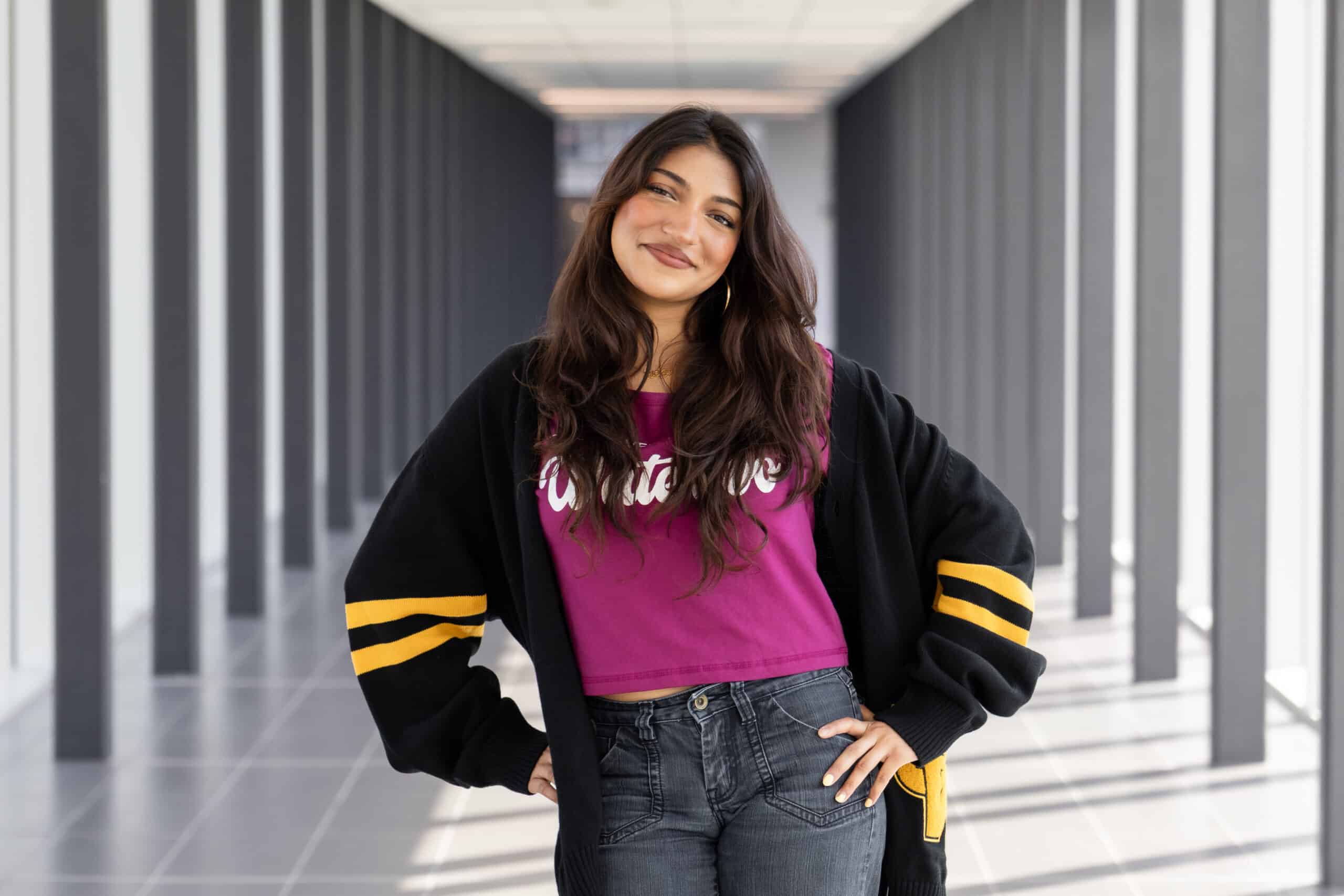 Smiling woman in a magenta shirt and black cardigan stands in a bright hallway with hands on hips, exuding the confidence of someone ready to step onto the stage of The Musical.