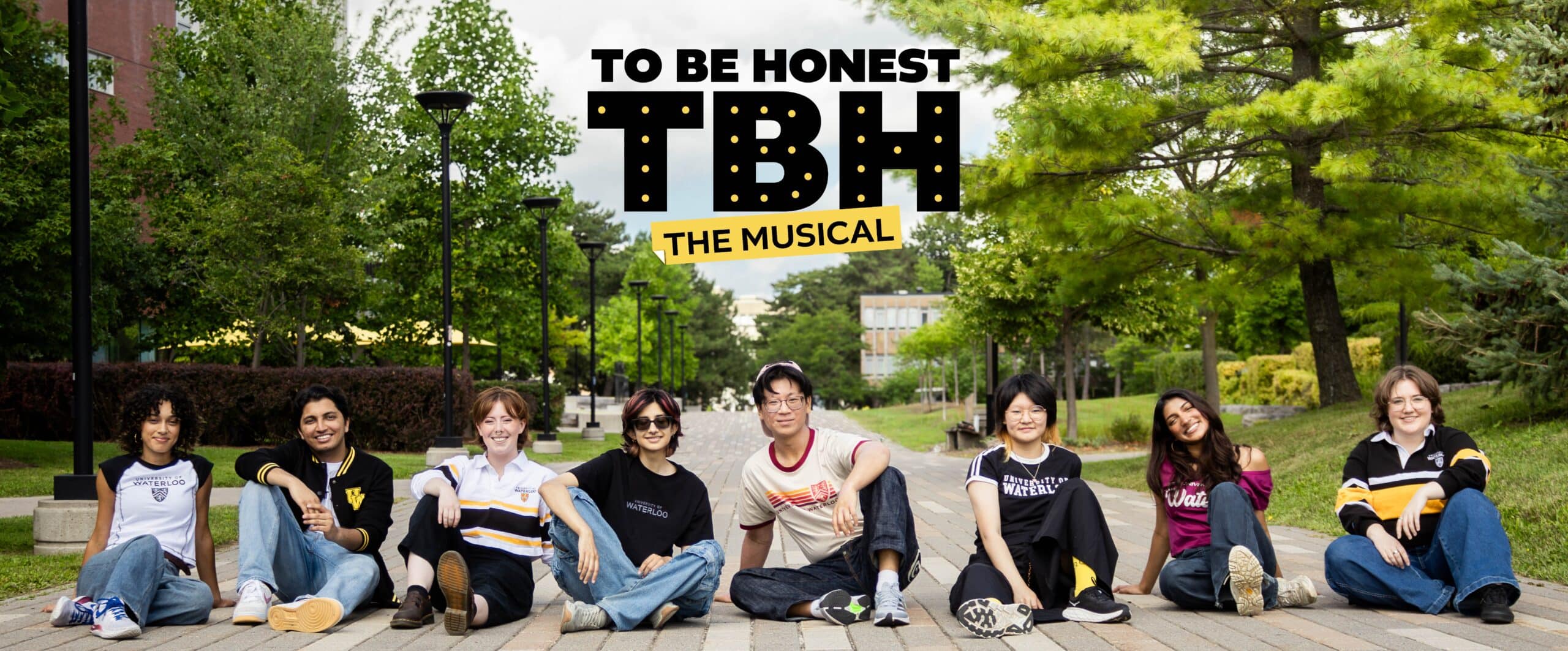 Eight students sit on a path outdoors under trees, smiling, with “TBH: The Musical” text above them.
