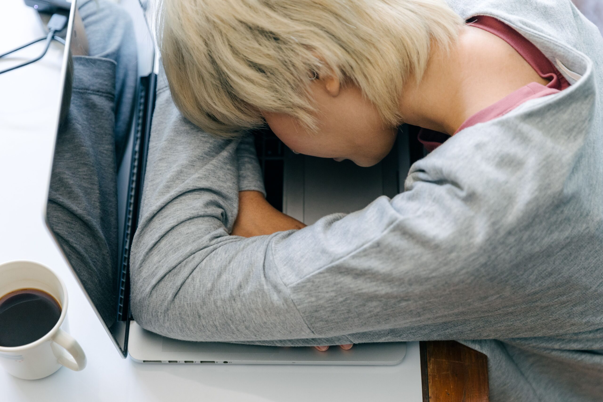 A person with short blonde hair sleeping on an open laptop, reflecting the struggles of burnout.
