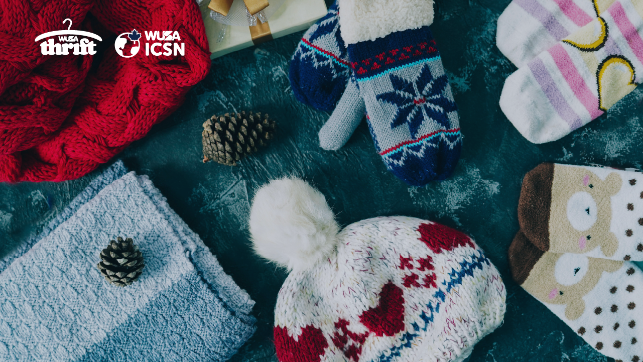 A knit hat, patterned mittens, and fuzzy socks with pinecones on a dark surface for a Winter Warm-Up community event.