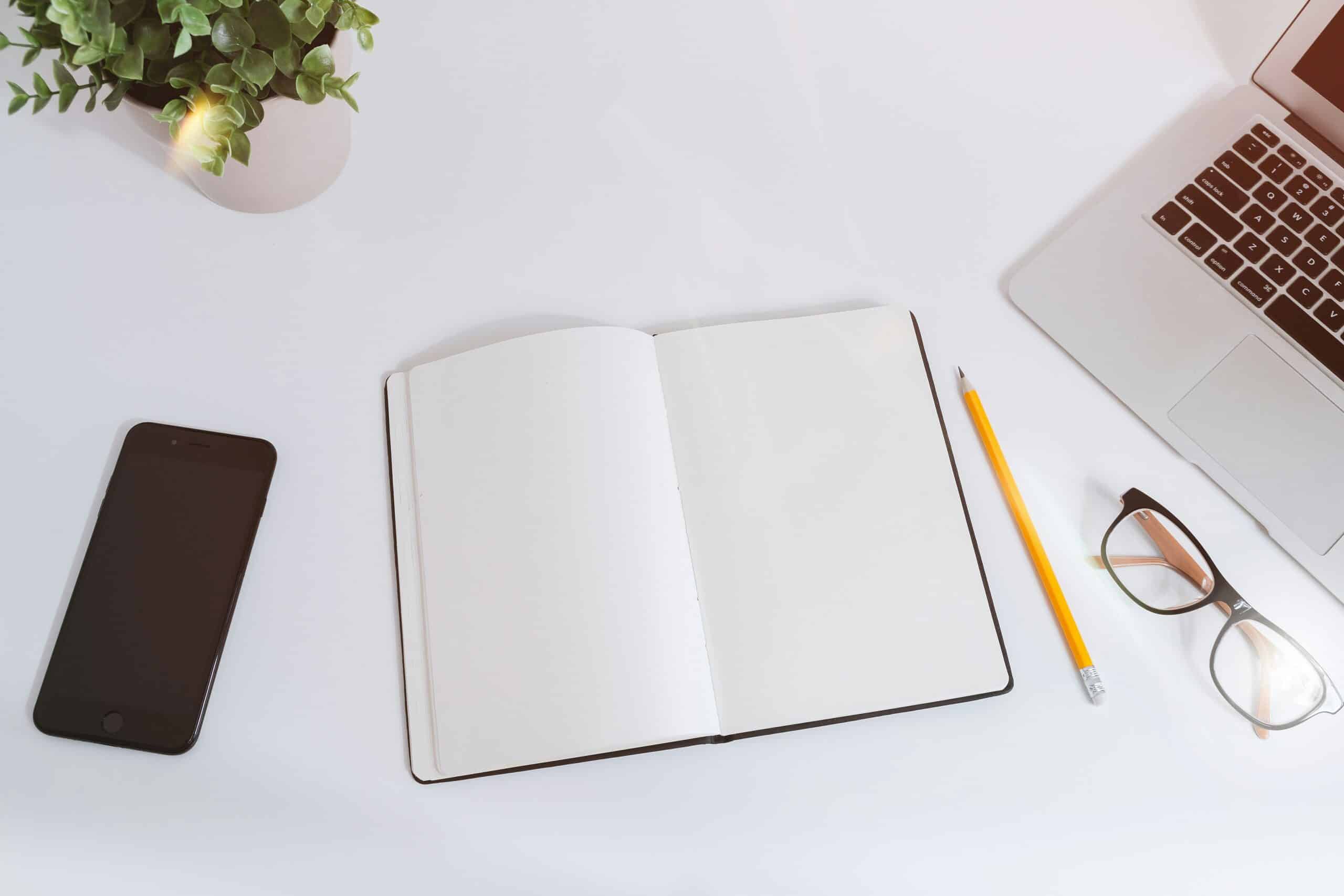 An open notebook for Reading Week study tips sits on a desk with a laptop, smartphone, glasses, pencil, and a plant.