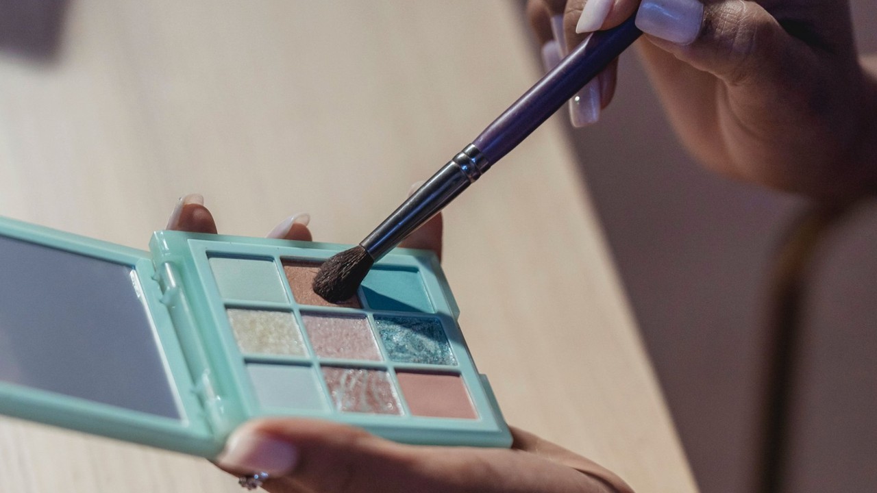 A makeup brush picking up eyeshadow from a nine-pan palette during a glow makeup workshop.